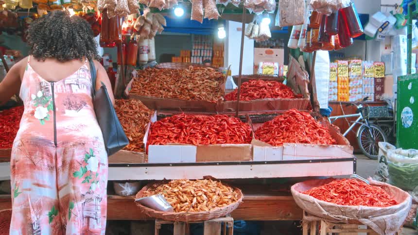 A woman holding a handbag buys seafood from an open street market shop at midday