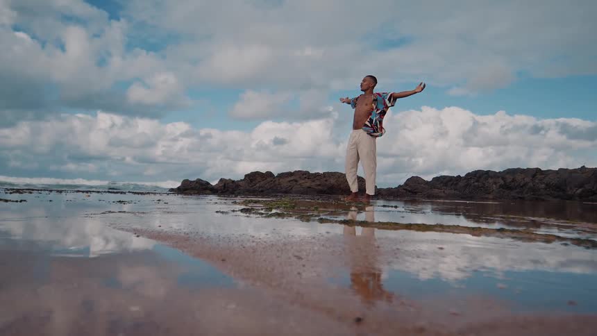 Man stands joyfully on a rocky beach with arms open wide