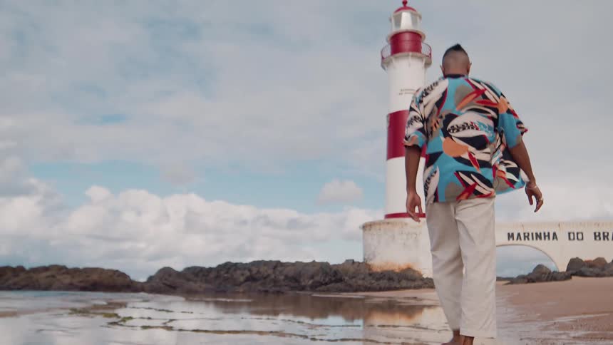 Man joyfully walks near a coastal lighthouse under a bright sky