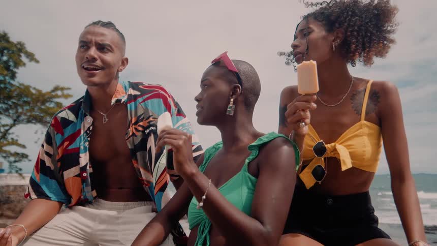 Three friends enjoy ice cream and chat by the seaside on a sunny day