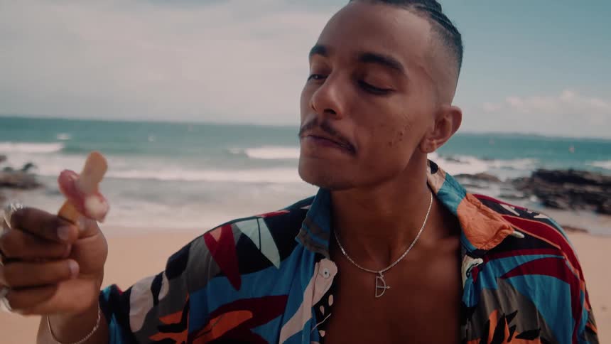 The face of a man who is eating a popsicle on a stick and he is on a beach