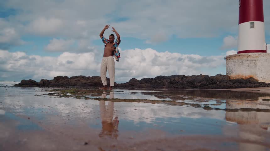Man stretching and standing by a lighthouse on a reflective beach at low tide