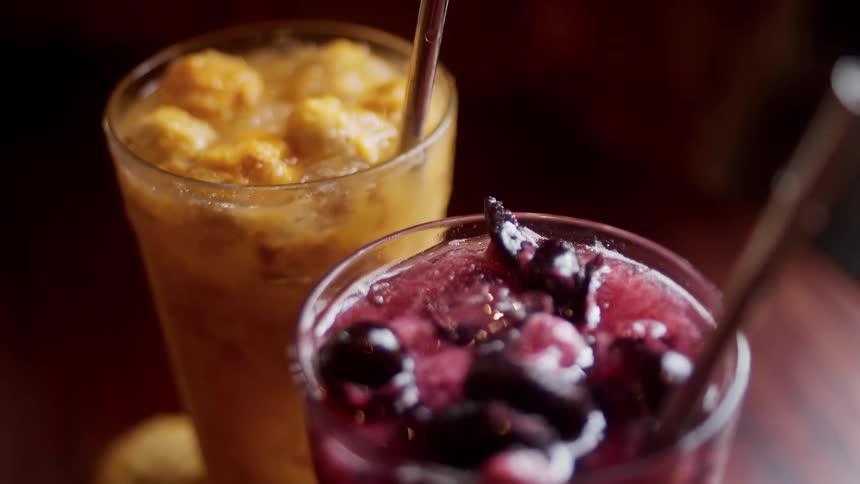 Closeup of orange and purple iced drinks with fruit and metal straws