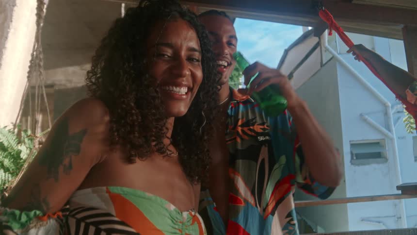 A group of friends in colorful clothes stand together holding beer bottles laughing and enjoying the moment in a tropical setting