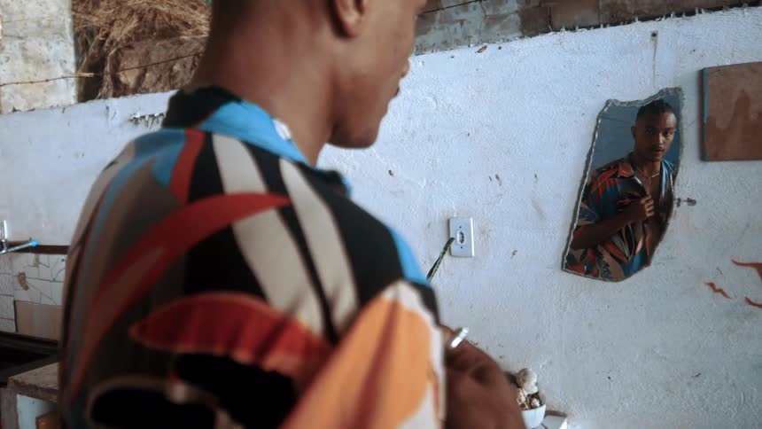 A man puts on a shirt while looking in the mirror