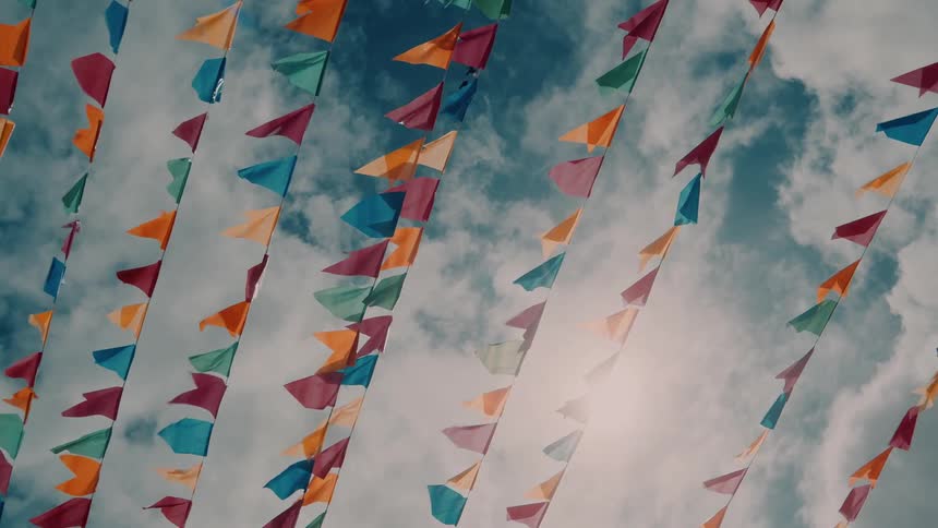 Colorful pennant flags swaying with wind under blue skies and white clouds
