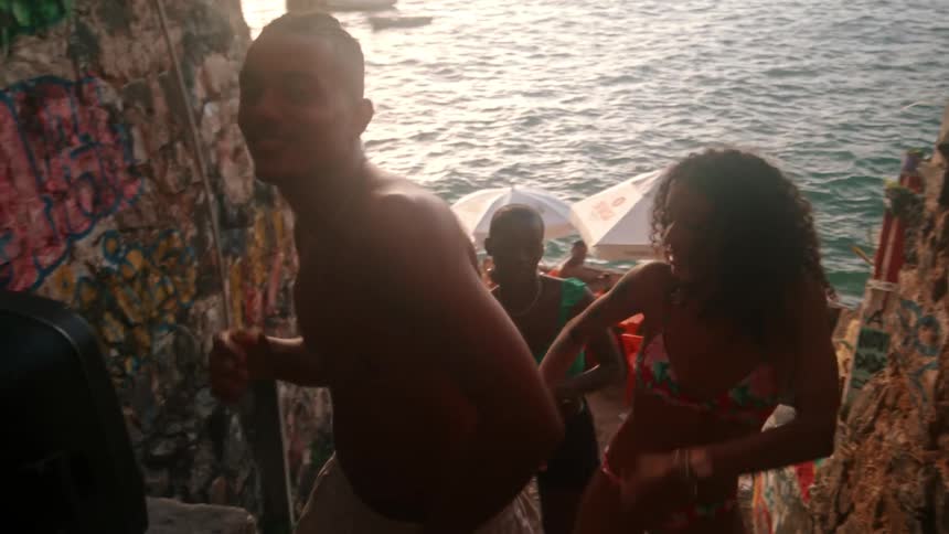 Young people in swimsuits dance and smile near the ocean at sunset