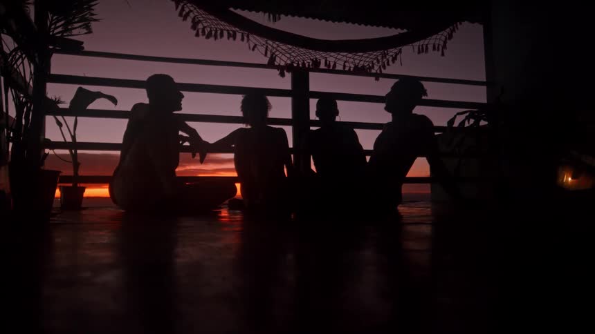 Silhouette of four people sitting on an outdoor porch at dawn with a red sky