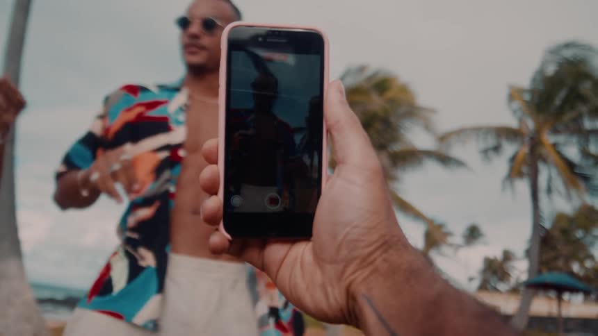 Close up of a persons hand recording a group of black friends dancing at the beach during daytime