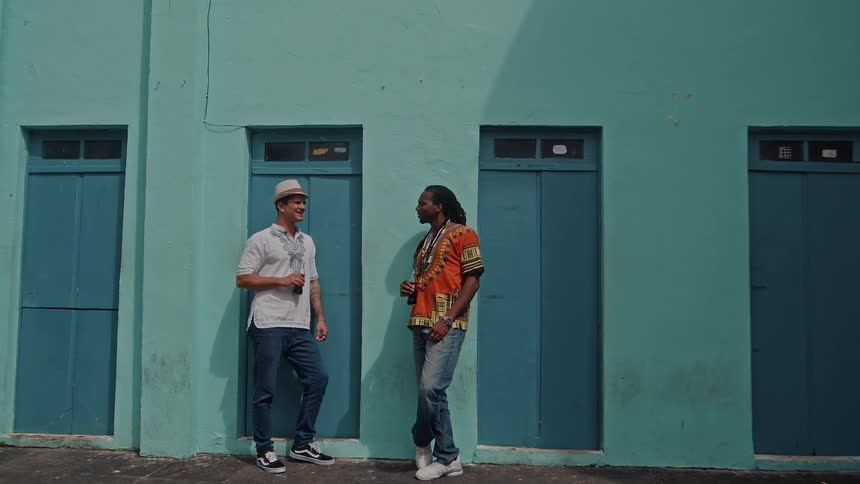 Two men chat and smile while standing outside a turquoise building