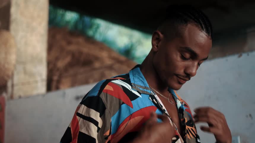 A young black man dressed in summer clothing wearing a silver necklace and rings on his fingers