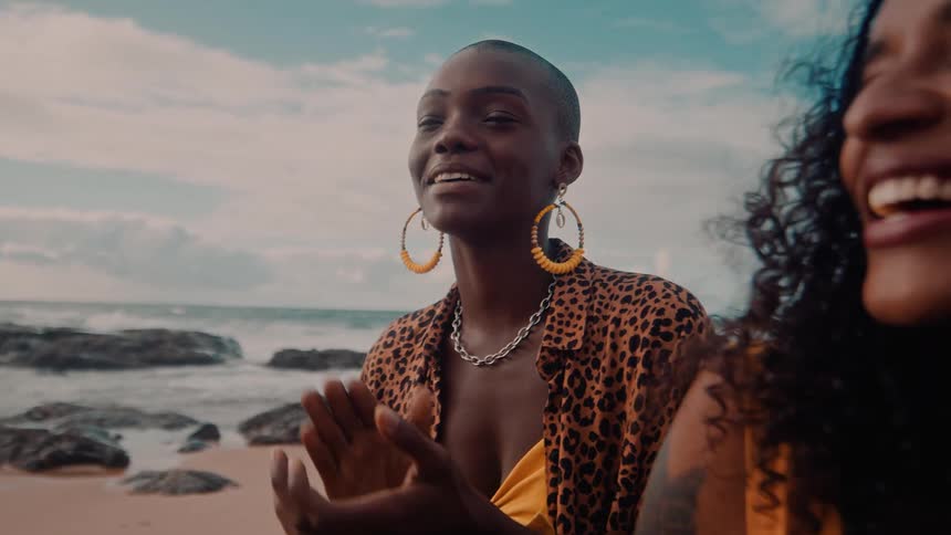 Two smiling women sitting on rocks on a beach