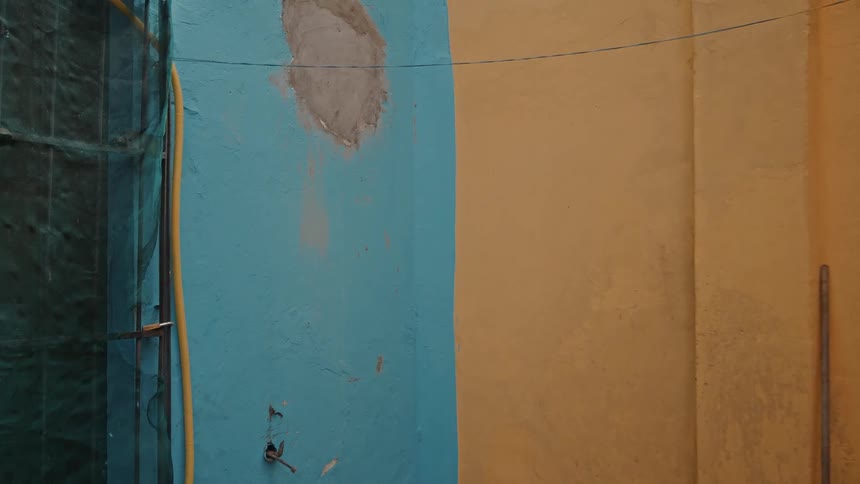 A static shot captures the corner of a weathered urban building with a patched bright blue wall next to a mustardyellow wall