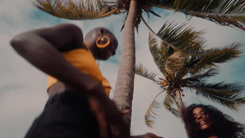 People smile while dancing together outdoors near a palm tree on a summer day