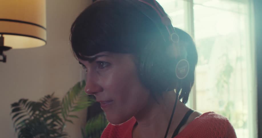 The woman puts on her headphones and plays a video game