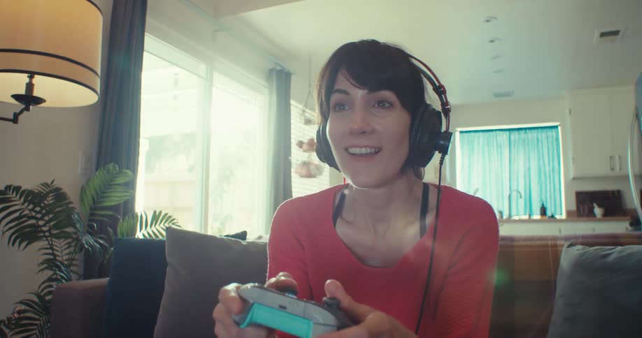Woman plays video games with headphones on in a bright living room