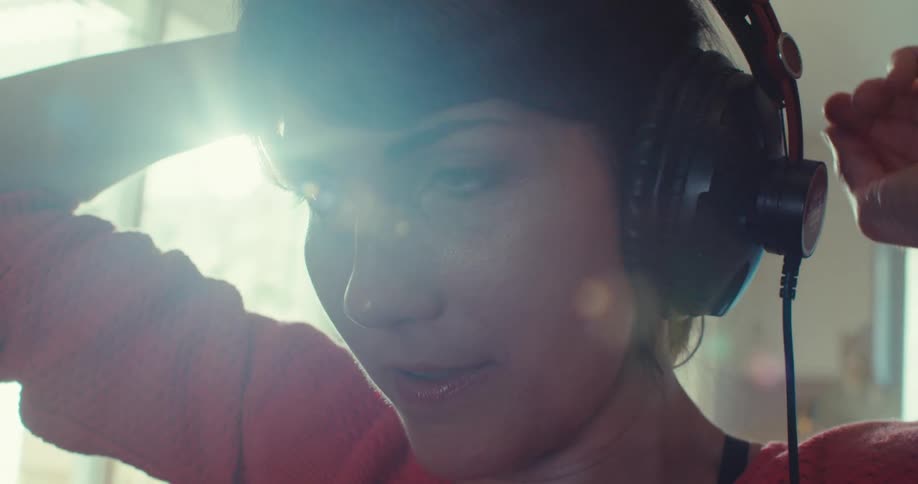 A woman wearing a red outfit and headphones on her head is tying her ponytail while talking