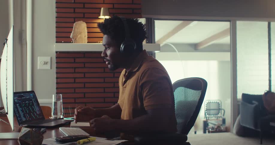 A man wearing headphones gestures while on a video call at his desk
