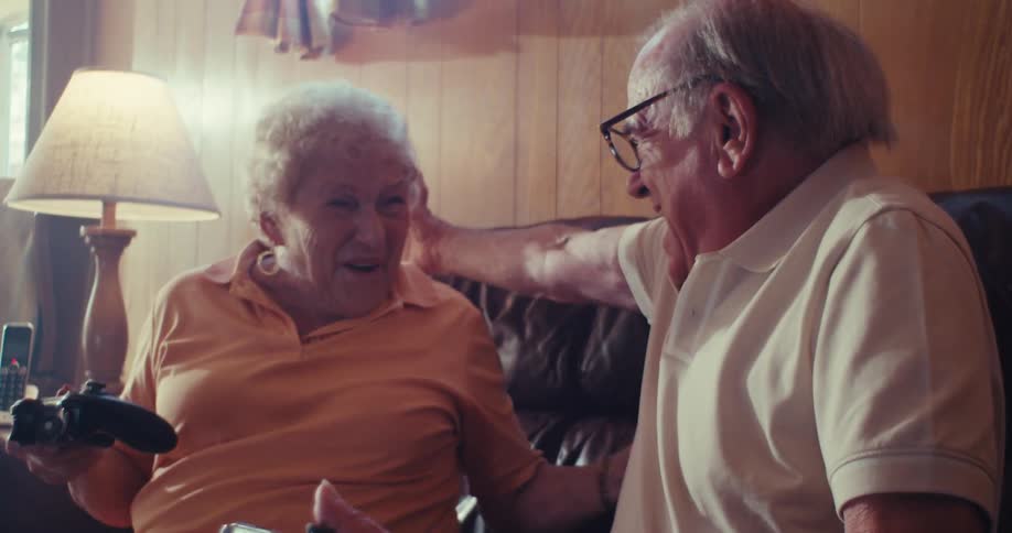 Two elderly couple joyfully sit on a couch playing video games together