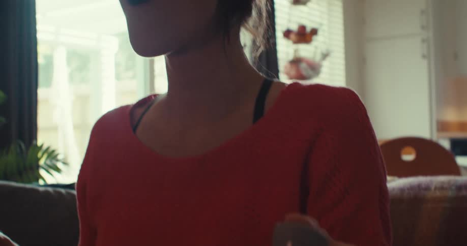 The woman is smiling and waving the controller on the couch