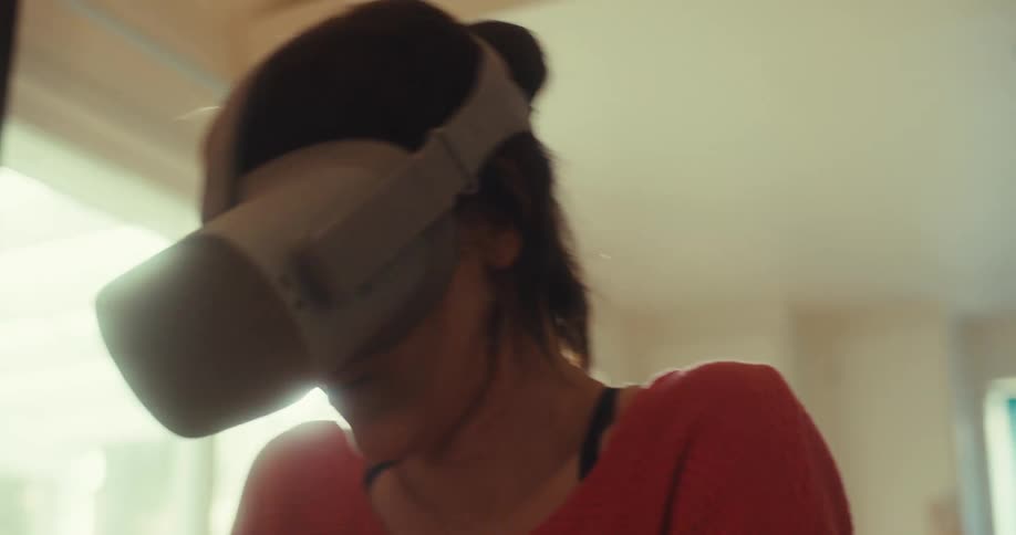 A woman plays with a vr headset indoors lit by bright sunlight