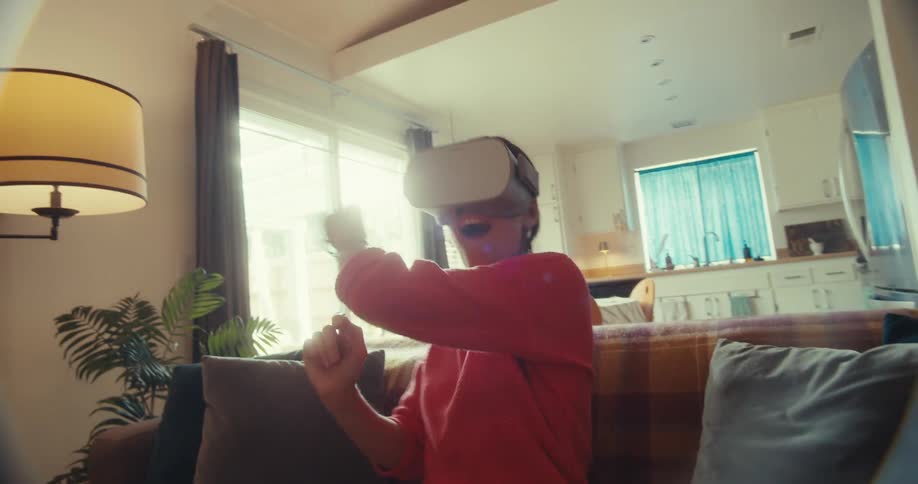 A woman wearing a vr headset sits on a living room couch interacting with her virtual environment