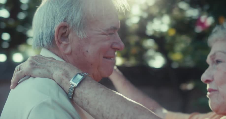 An elderly couple dancing outdoors under sunlight