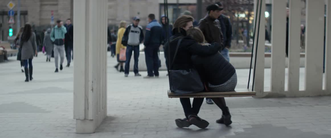 Two people are sitting hugging in a busy square