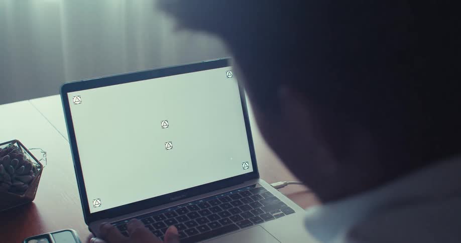 A man sits at a desk using a laptop with a blank placeholder screen