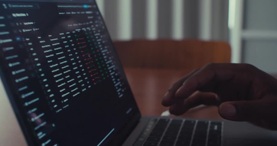 A black man smiles while typing on a laptop computer indoor at daytime