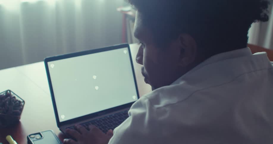 Man works on a laptop at a desk in a softly lit room