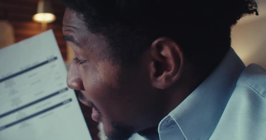 A man reviews his portfolio holdings on a printed document expressing concern as he discusses the numbers during a video call