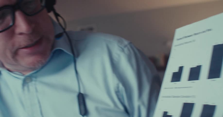The man talks while pointing at a graph on a paper