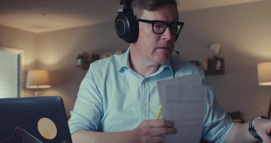 A man on a video call explains data by pointing at a printed chart