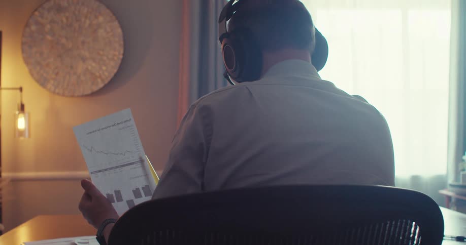 Man in headphones examines printed graphs at a desk in a softly lit office