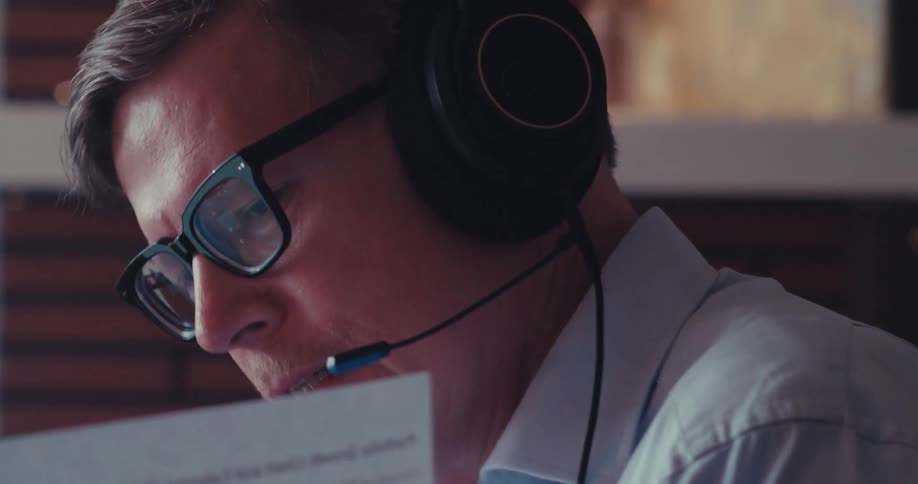 The man is reading a paper and talking into the mic on his headset