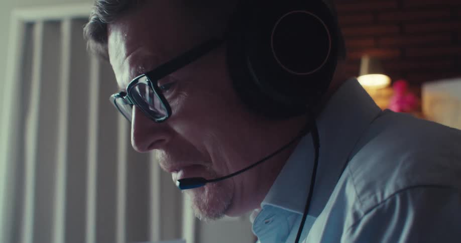 A person wearing headphones and a light blue shirt sits in a home office going over documents and explaining their contents