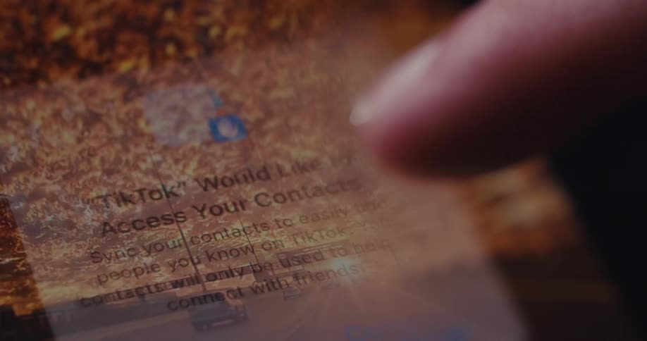 In a closeup a finger hovers over a smartphone screen showing permission requests from the tiktok app to track activity and access contacts