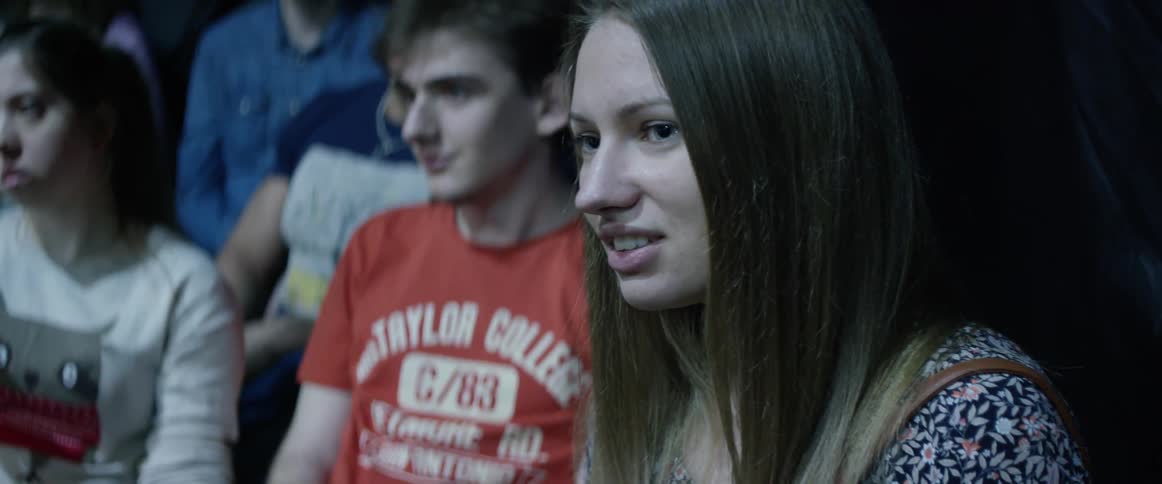A woman sitting in a crowd is watching and listening to something