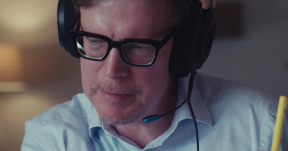 A man wearing headphones holds a graph filled document while explaining it during a call