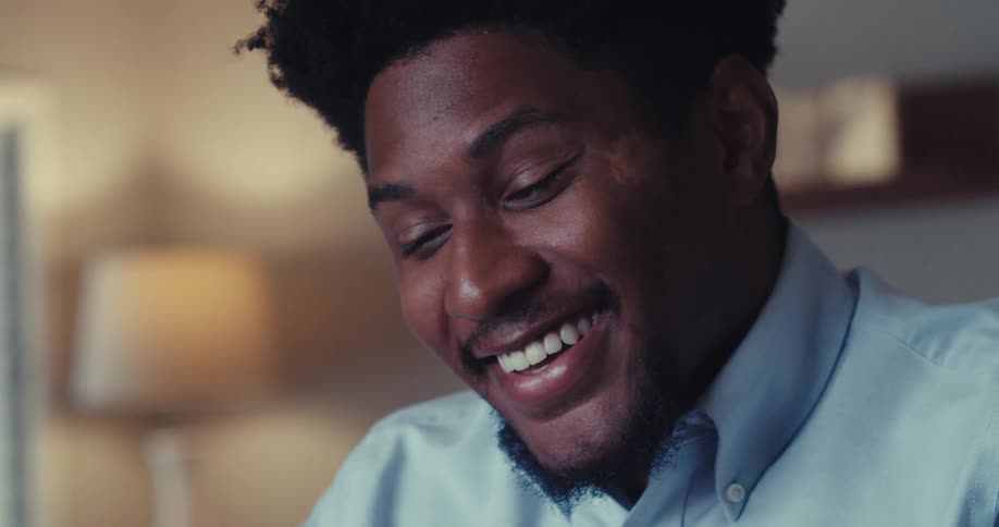 A young man sits suddenly gets excited leans back and begins to laugh
