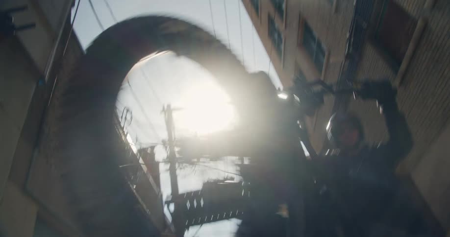 A cyclist pops a spinning wheelie in a sun-soaked urban alley silhouetted against the bright sky