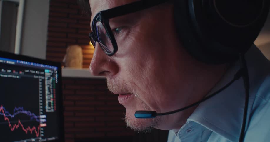 A man wearing headphones analyzes stock charts on multiple screens during a work call