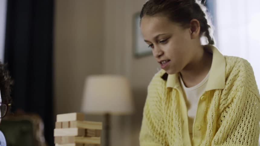 A mother and daughter play a game of jenga in their living room enjoying a fun time together