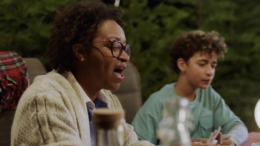 Family plays cards outdoors while the father operates the grill