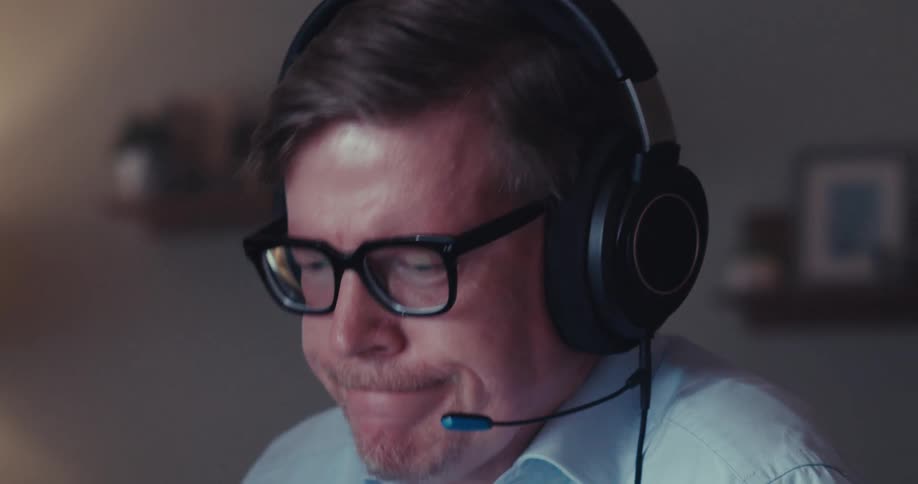 A mans face wearing headphones and he is talking while smiling and wearing glasses