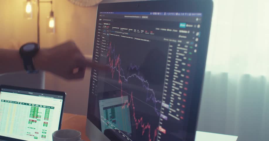 Person points at a fluctuating stock chart on a computer monitor