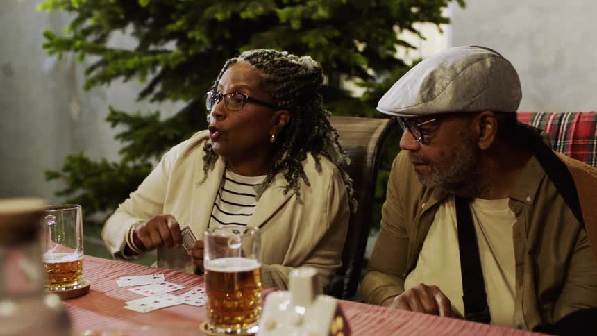 An older couple joyfully plays cards at an outdoor dinner table celebrating with a high five while a young girl snacks on popcorn nearby