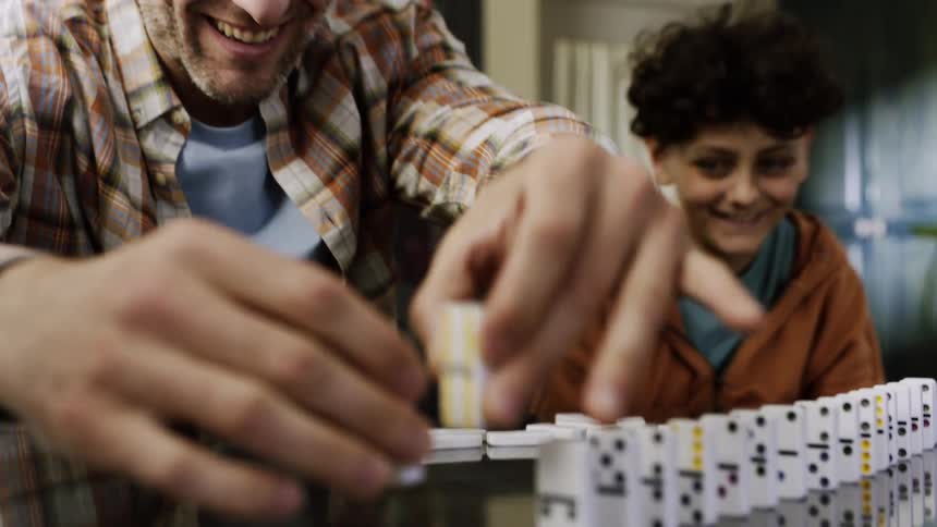 Father and son play with dominoes at a table sharing a playful moment
