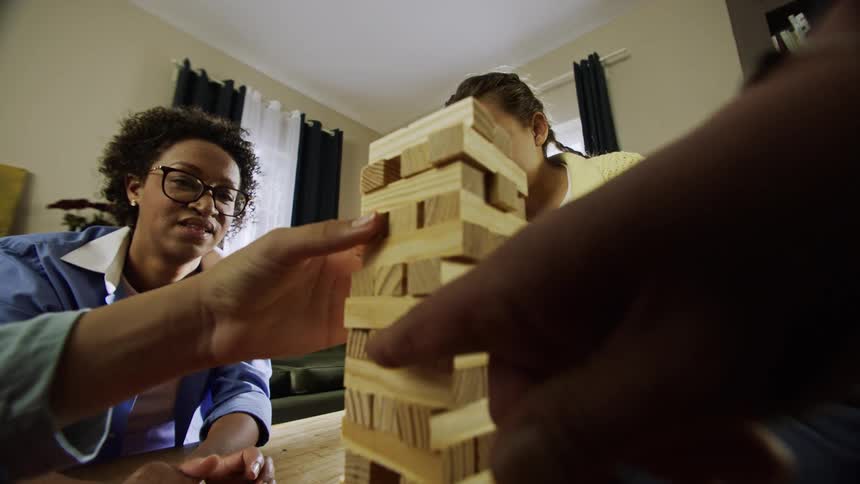 A family plays a game of jenga carefully pulling and stacking wooden blocks on a small table
